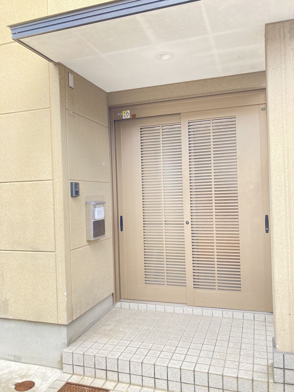 玄関まわりの写真。タイル敷きのアプローチの奥に引き戸の玄関があり、左側にインターホンとポストが設置されています。