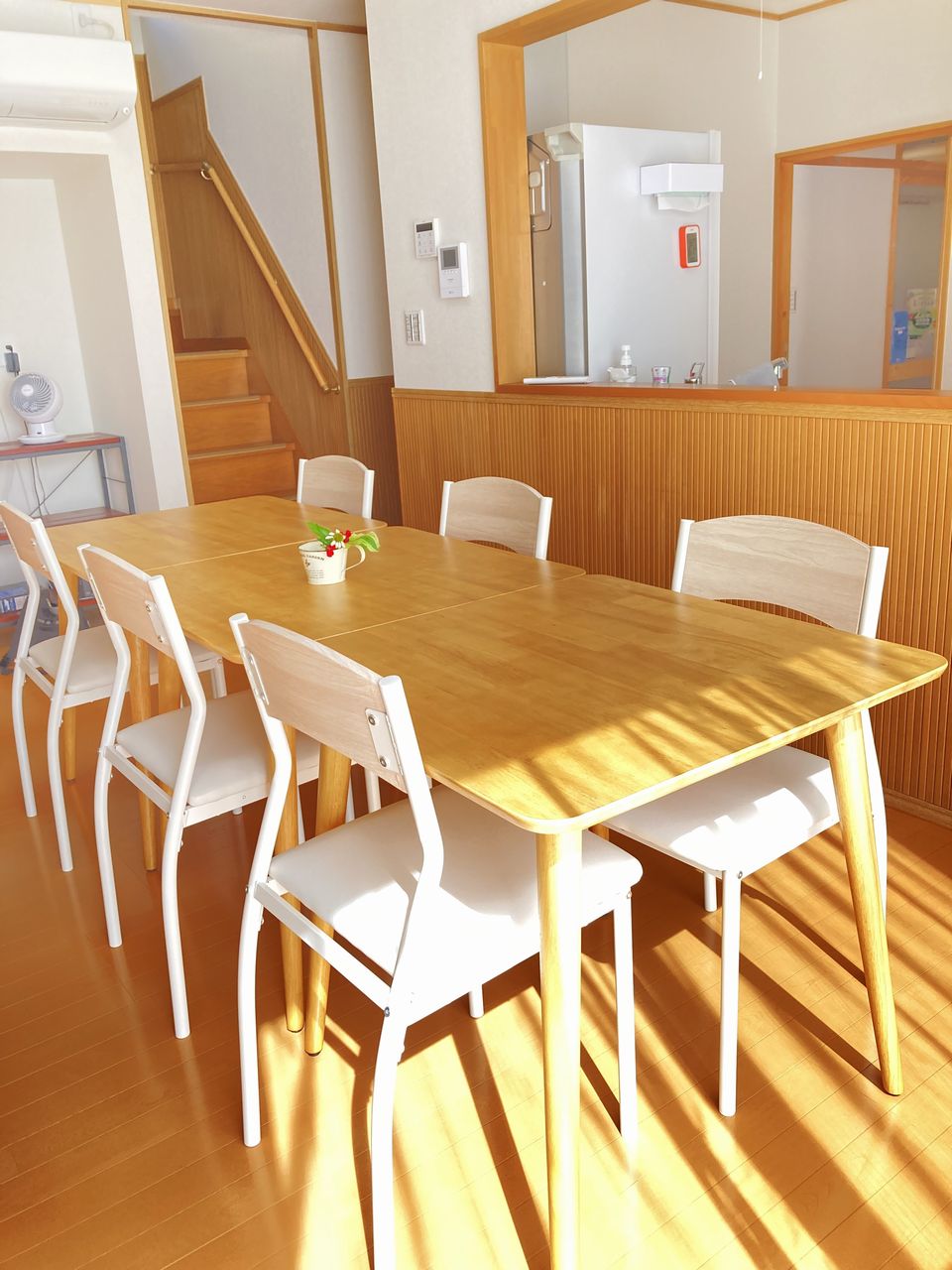 リビング・ダイニングの別角度の写真。テーブルの奥にカウンターがあり、左手に階段、右手奥にキッチンへ続く開口部が見えます。