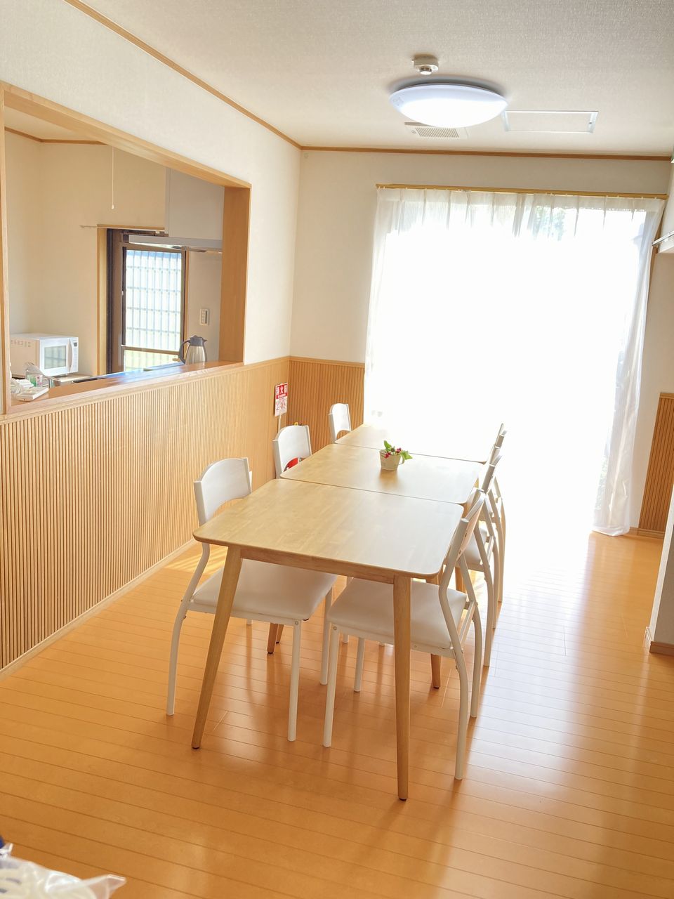 リビング・ダイニングの写真。木目の床にダイニングテーブルと椅子が並び、右側の大きな窓から日光が入る明るい空間です。