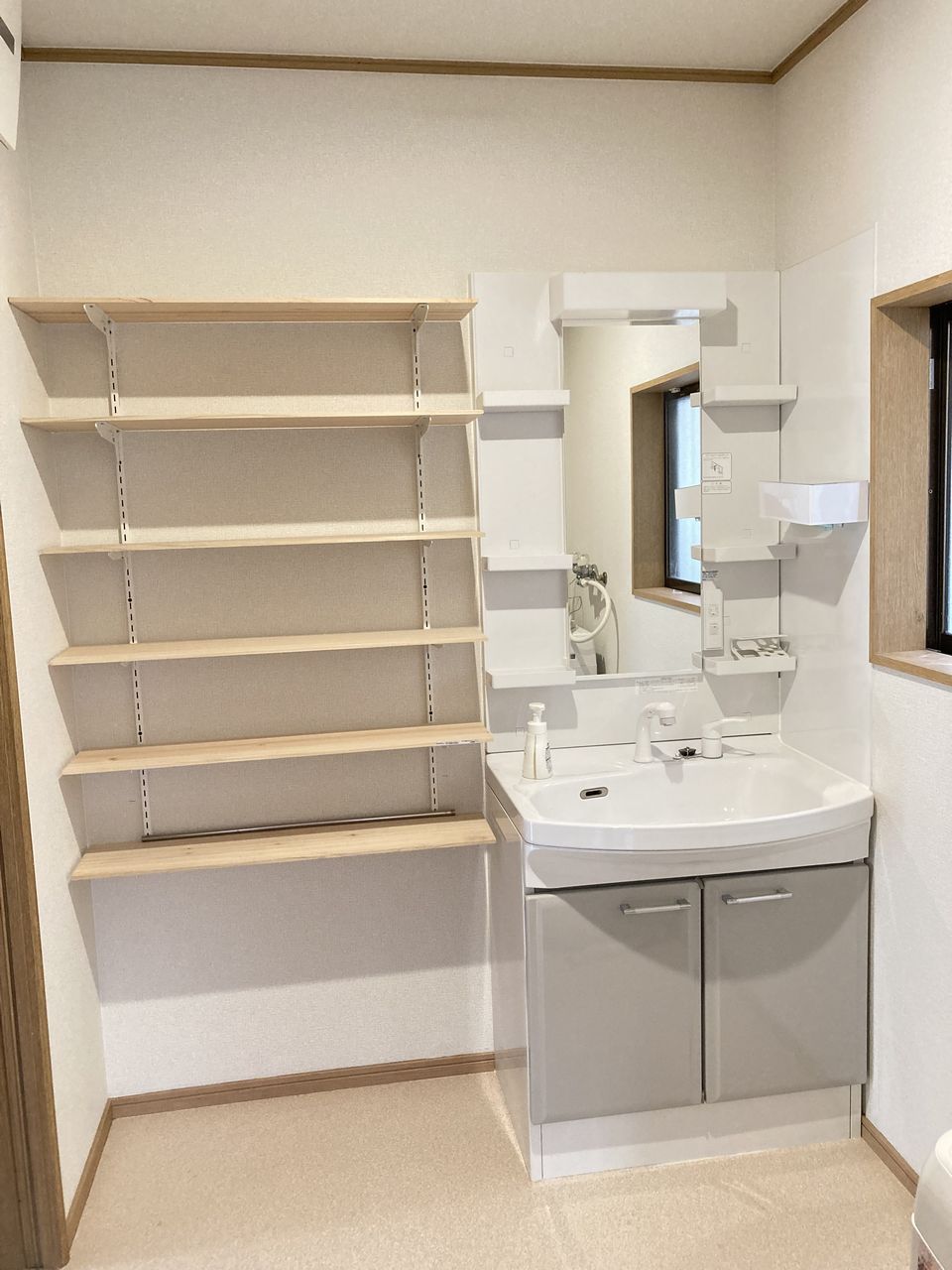 洗面所の写真。洗面台と鏡、収納棚があり、横に窓がある明るいスペースです。